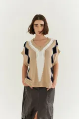 Chaleco de punto color beige con diseño de rombos negros y blancos, bordado a mano y detalles de lurex. Tiene cuello en V y sisas amplias.