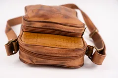 Bandolera de cuero color terracota con correa ajustable, cierre superior y bolsillo externo con cierre. Incluye bolsillo interno y logo de la marca en el frente.