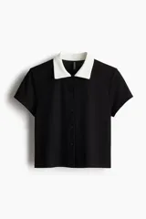 Camisa negra de punto acanalado con cuello blanco, manga corta y botonadura frontal.
