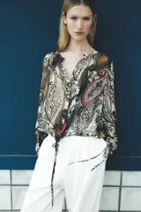 Blusa semitransparente de cuello redondo y manga larga con lazadas ajustables en los puños. Tiene bajo ajustable con lazada y cierre frontal con botones ocultos.