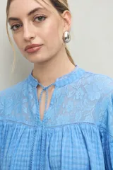 Blusa blanca de algodón con encaje floral en la parte superior, mangas largas abullonadas y escote con lazo.