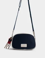 Bandolera de cuerina azul marino y beige con correa regulable azul y charm lateral decorativo. Tiene cierre superior y tag frontal con logo "The Brunch Club".