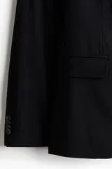 Blazer negro de corte slim fit, con solapas de muesca finas y ojal decorativo. Modelo de botonadura sencilla con bolsillo superior insertado, bolsillos delanteros con solapa, dos bolsillos en el interior y botones decorativos en los puños. Abertura doble atrás.