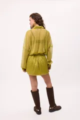 Vestido corto color verde lima, estilo camisero, confeccionado en chiffon transparente. Tiene cuello camisero, mangas largas abullonadas y elástico en la cintura.