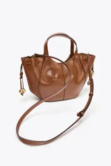 Bolso de mano color marrón con detalle de pespuntes en el cuerpo y tiradores laterales con abalorios en efecto metalizado. Tiene doble asa de mano y correa extraíble para usar como bandolera. Incluye cartera interior con cierre de cremallera y cierre imantado.