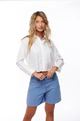 Camisa blanca de manga larga con cuello clásico y cierre frontal con botones. Presenta detalle de calado en el ruedo.