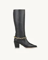 Bota alta de cuero negro con punta fina, taco geométrico y detalle de cadena dorada en el tobillo.