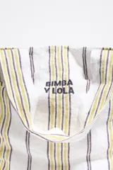 Bolso tipo shopper de lona color crudo con rayas verticales amarillas y grises. Tiene doble asa de hombro y logo de la marca estampado en el frente.