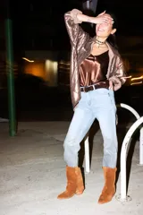 Pantalón de jean celeste claro, corte boyfriend, con laminado dorado en la parte inferior de la pierna y cinturón de cuero marrón.