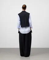 Chaleco sastrero sin mangas, color azul marino, con solapas de traje, cierre frontal de botón oculto y bolsillos de vivo en el pecho y la cadera. Presenta aberturas laterales y espalda corta.