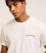 Remera de algodón color crudo, de corte recto y manga corta. Presenta un pequeño estampado con texto "Hawaiian Islands" en el pecho.