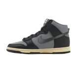Zapatillas Nike Dunk High Retro, color gris y negro, con suela color crema y detalle de dije dorado en forma de llave.