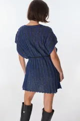 Vestido corto de tejido de punto con cuello V y mangas cortas, con diseño de rayas verticales en tonos azul oscuro y negro, con hilos de lurex que le dan brillo. Se ajusta a la cintura con un lazo fino negro.