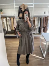 Vestido camisero largo color gris topo, de pana fina con línea italiana, cuello mao, cierre frontal con botones, mangas largas con puños abotonados, dos bolsillos de parche en el pecho, cintura ajustable con cordón y falda recta.