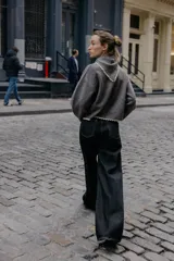 Chaqueta de punto gris oscuro, corte cropped y manga larga, con cuello redondo que incorpora una bandana anudada al frente. Los bordes del cuello, puños y ruedo están terminados con una puntilla de encaje color beige claro. Cierre frontal con botones oscuros.