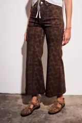Pantalón de jean tiro medio, corte wide leg acampanado, color marrón oscuro con estampado animal print en tonos más oscuros y pequeños puntos rosados.