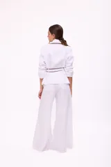 Pantalón de tiro alto, corte ancho y largo, color beige claro con finas rayas verticales en tono oscuro. Presenta cierre frontal con botón y bolsillos tipo jean.