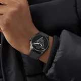 Reloj analógico Guess modelo Clark, con caja redonda negra y correa de silicona negra. La esfera negra presenta un gran triángulo plateado con diseño geométrico en su interior, y las agujas son plateadas.