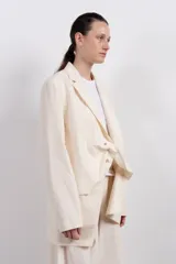 Blazer color crema de corte amplio con diseño asimétrico y detalle de nudo frontal.