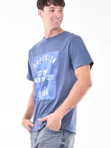 Remera blanca de corte recto con estampa fotográfica de edificios en la parte frontal.