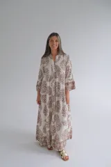 Vestido largo color blanco con estampado floral marrón, cuello mao y mangas 3/4 con volados. Diseño amplio con corte en la cintura y falda escalonada. Cierre frontal con botones.