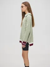 Sweater de punto color verde claro con cuello polo con cierre de cremallera, mangas largas y diseño con trenzas. Puños acanalados con rayas en color borgoña y blanco.