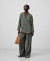Blusa verde oliva de tejido arrugado con poliéster reciclado. Escote pico, manga japonesa, delantero cruzado y ata lateralmente con tira estrecha del mismo tejido.