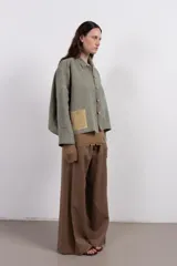 Camisa amplia de lino en tono verde desgastado, con textura visual y caída liviana. Destaca por su parche tejido a mano en contraste, que aporta un detalle artesanal y único.