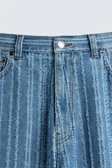 Pantalón de jean azul con rayas verticales texturadas, corte relaxed fit, cinco bolsillos, efecto lavado y cierre frontal con cremallera y botón.