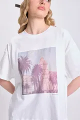 Remera blanca de corte cuadrado con estampa fotográfica de palmeras y edificio.