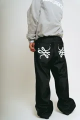 Pantalón de jean negro de corte baggy, con estampado de trigramas blancos en los bolsillos traseros.
