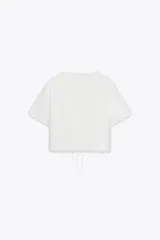Camisa blanca de manga corta con escote en pico y cierre frontal con lazadas. Presenta bordados florales a tono.