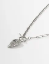 Collar de acero quirúrgico plateado con cadena de eslabones tipo cubana y cadena de eslabones alargados. Cierre tipo toggle con barra y anillo. Dije colgante con forma de corazón alargado con grabado.