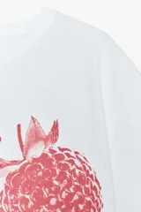 Camiseta blanca de algodón con cuello redondo y mangas cortas. Estampado frontal con texto "Sweet Berry" y dibujo de frambuesas en color rojo.