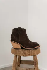 Bota corta de gamuza color marrón oscuro, con puntera cuadrada y detalles de costuras decorativas. Tiene un taco de madera con forma cónica.