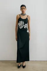 Vestido largo negro de breteles finos, con escote redondo y detalle de apliques florales blancos en el frente.