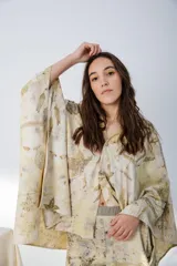 Vestido corto con estampado de hojas en tonos beige y amarillo, sin mangas y escote redondo. Incluye un poncho a juego con el mismo estampado.