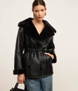 Blazer negro confeccionado en material sintético PU, con cuello y puños de piel sintética, cierre por cremallera y cinturón con hebilla en la cintura.