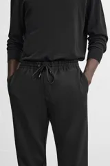 Pantalón negro de corte cropped, con cintura elástica ajustable con cordón, bolsillos laterales y traseros de vivo. El bajo tiene terminación con vuelta.