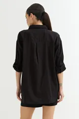 Camisa blanca de corte amplio, con cuello clásico, cierre frontal con botones y mangas largas con puños abotonados.