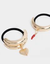 Set de dos gomitas de pelo elásticas negras con apliques metálicos dorados y dijes colgantes: una con dije de corazón y otra con dije de pimiento rojo.