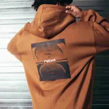 Sudadera con capucha (canguro) color mostaza, de corte holgado, con bolsillo canguro frontal y un pequeño parche estampado con el logo de la marca en el pecho izquierdo.