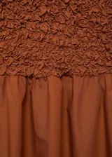 Vestido midi color marrón con textura arrugada en la parte superior y falda acampanada lisa. Sin mangas, con cuello redondo y espalda cerrada.