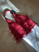 Chaleco de cuero color fucsia, estilo chaleco de flecos, con tachas metálicas plateadas en el frente. Posee un asa de hombro ancha.