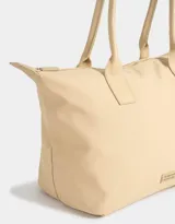 Bolso tipo shopper color beige con doble asa corta de hombro, cierre superior y tag de goma con logo.