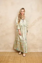 Vestido largo estilo hindú con estampado floral en tonos dorados y celestes, con bordados dorados, escote en V y mangas largas con volados y borlas decorativas.