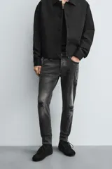 Pantalón de jean negro ajustado al cuerpo desde la cintura hasta el tobillo, de tiro medio y tejido elástico. Diseño de cinco bolsillos con lavado efecto roto y cierre frontal con cremallera y botón.