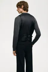 Chaleco de vestir negro con cuello en V, cierre de botones y bolsillos ribeteados. Espalda de tejido brillante con trabilla ajustable. Corte ajustado y forro interior.