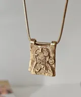 Collar dorado con dije rectangular con imagen religiosa y cristales azules.