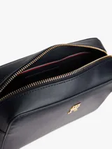 Cartera cruzada tipo cámara de poliuretano color azul marino, con cierre principal de cremallera y monograma TH metálico dorado al frente. La correa larga es ajustable y presenta la cinta distintiva de la marca en rojo, blanco y azul.